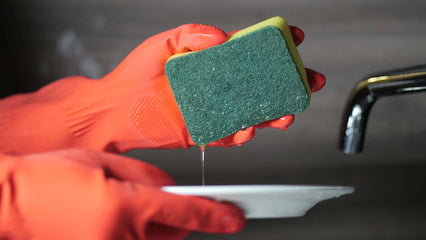person wearing orange gloves while cleaning the dishes