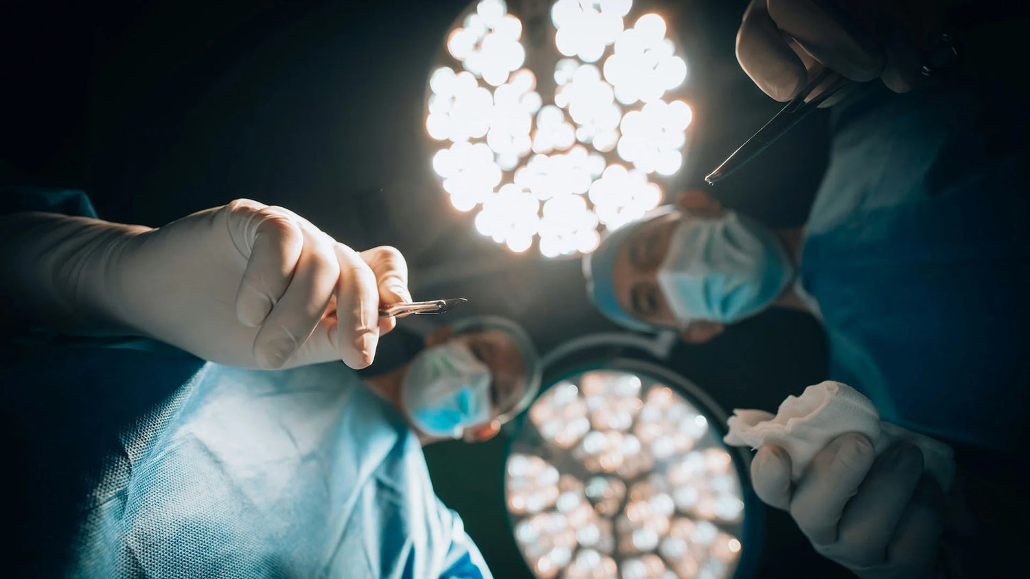View of a patient lying on the bed with the surgical team in personal protective equipments looking and a medical light above their heads.