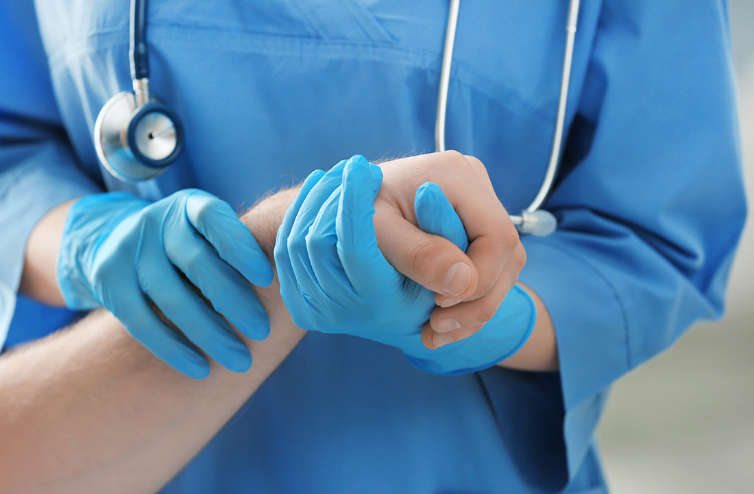 Person in scrubs and blue gloves holding patient's hand