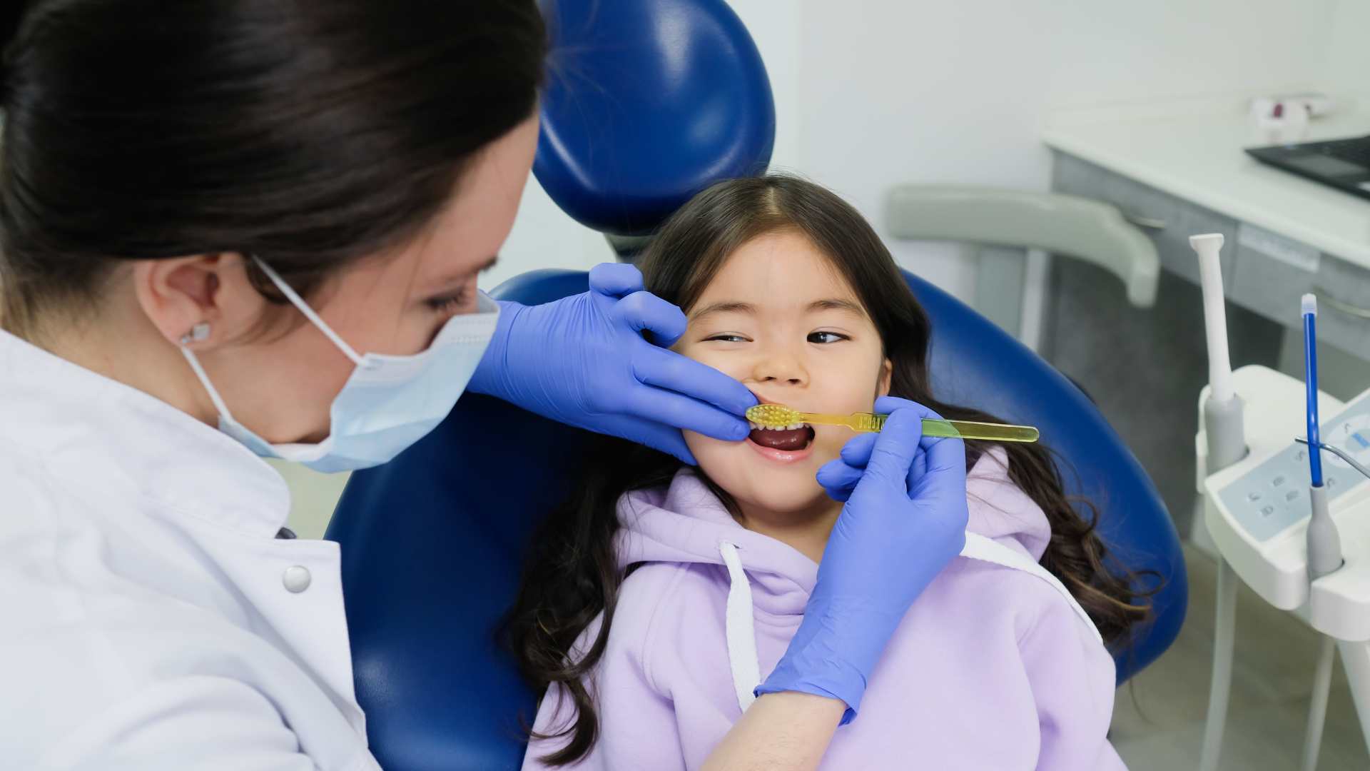 a dentist wearing gloves while brushing the teeth of a girl during a dental check-up