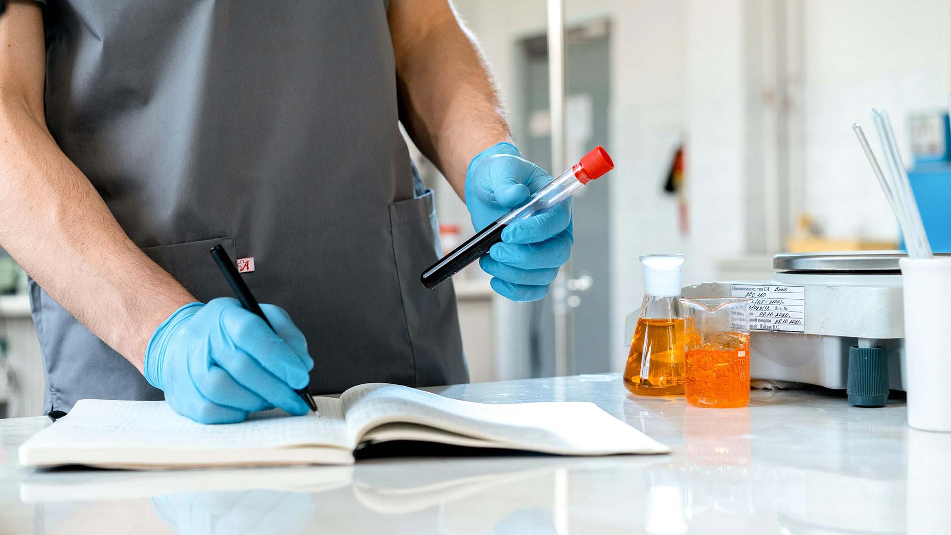 person writing while holding a test tube with liquid