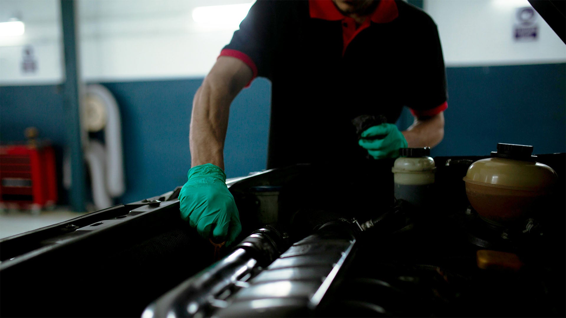 a mechanic wearing green gloves while inspecting a car's machine