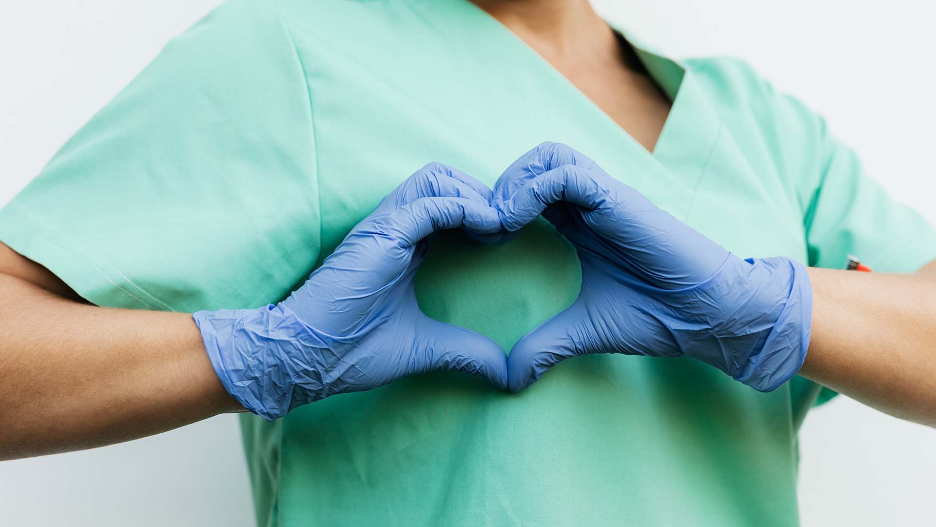 Person in scrubs making heart hands with gloved hands