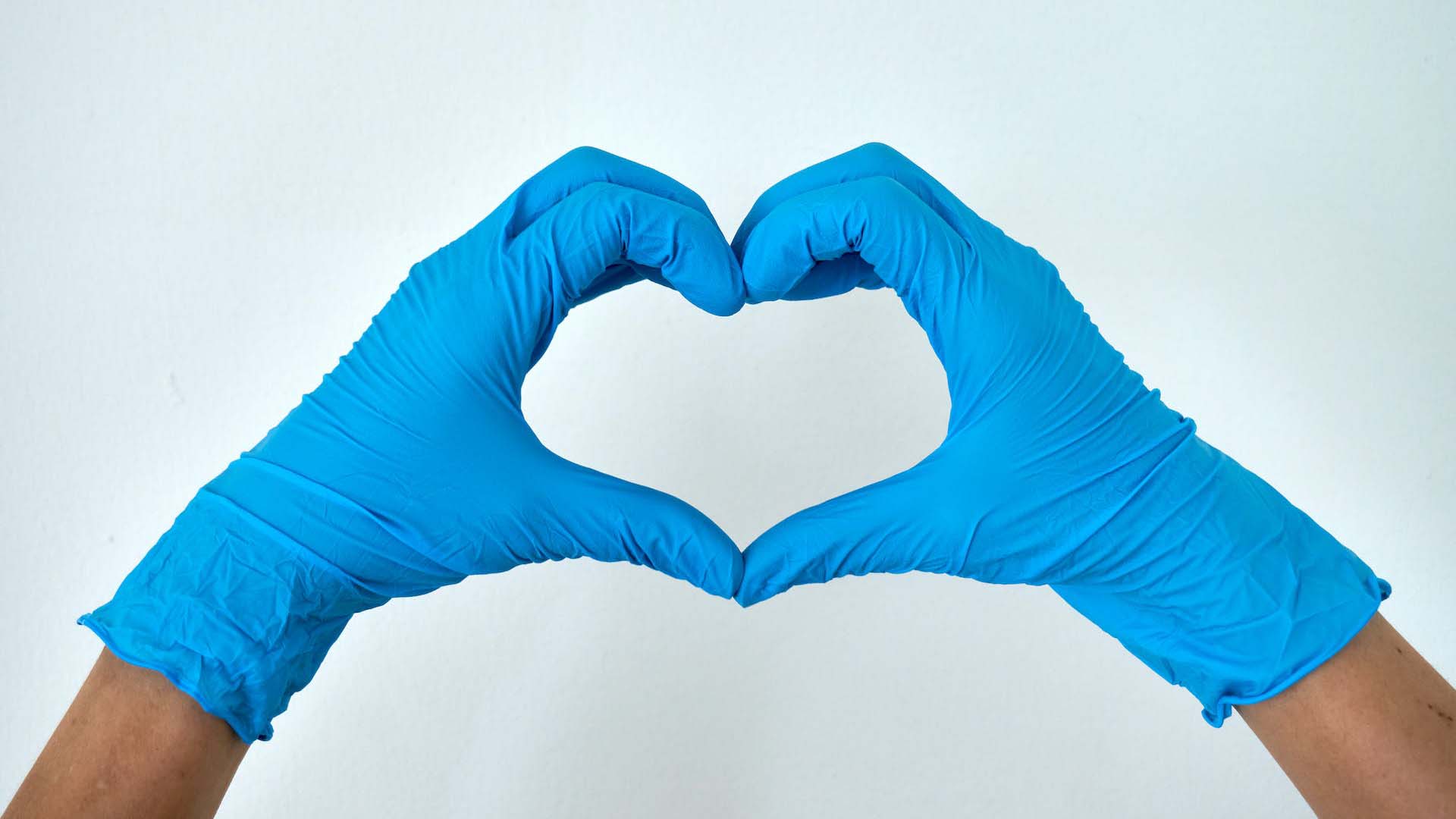 person wearing blue nitrile gloves making a heart sign 
