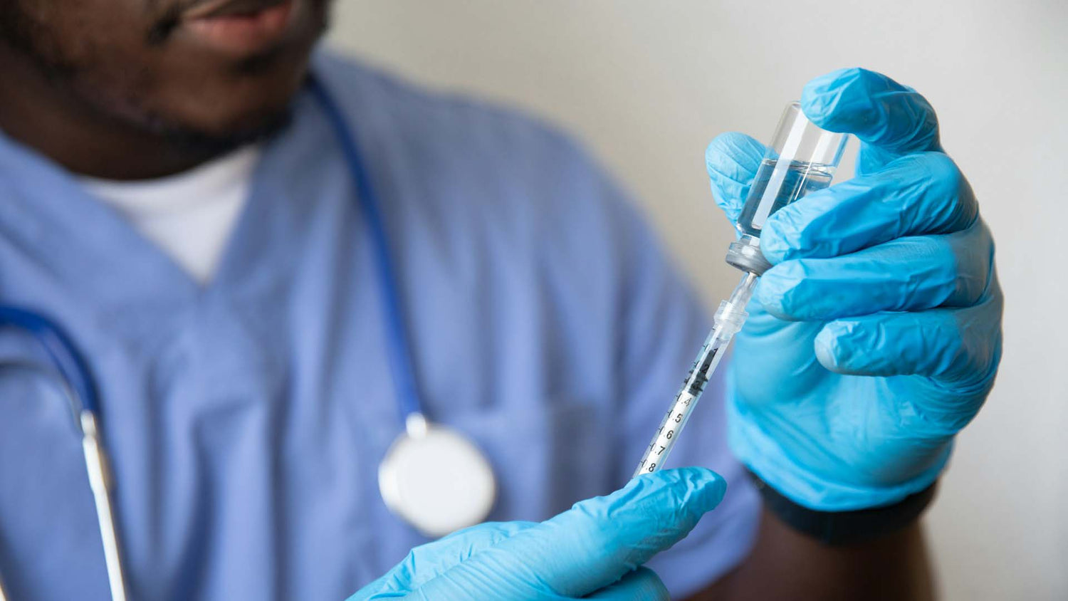 A doctor drawing a medication out of a vial using syringe while wearing medical gloves.