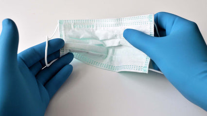 hands in blue gloves holding surgical mask