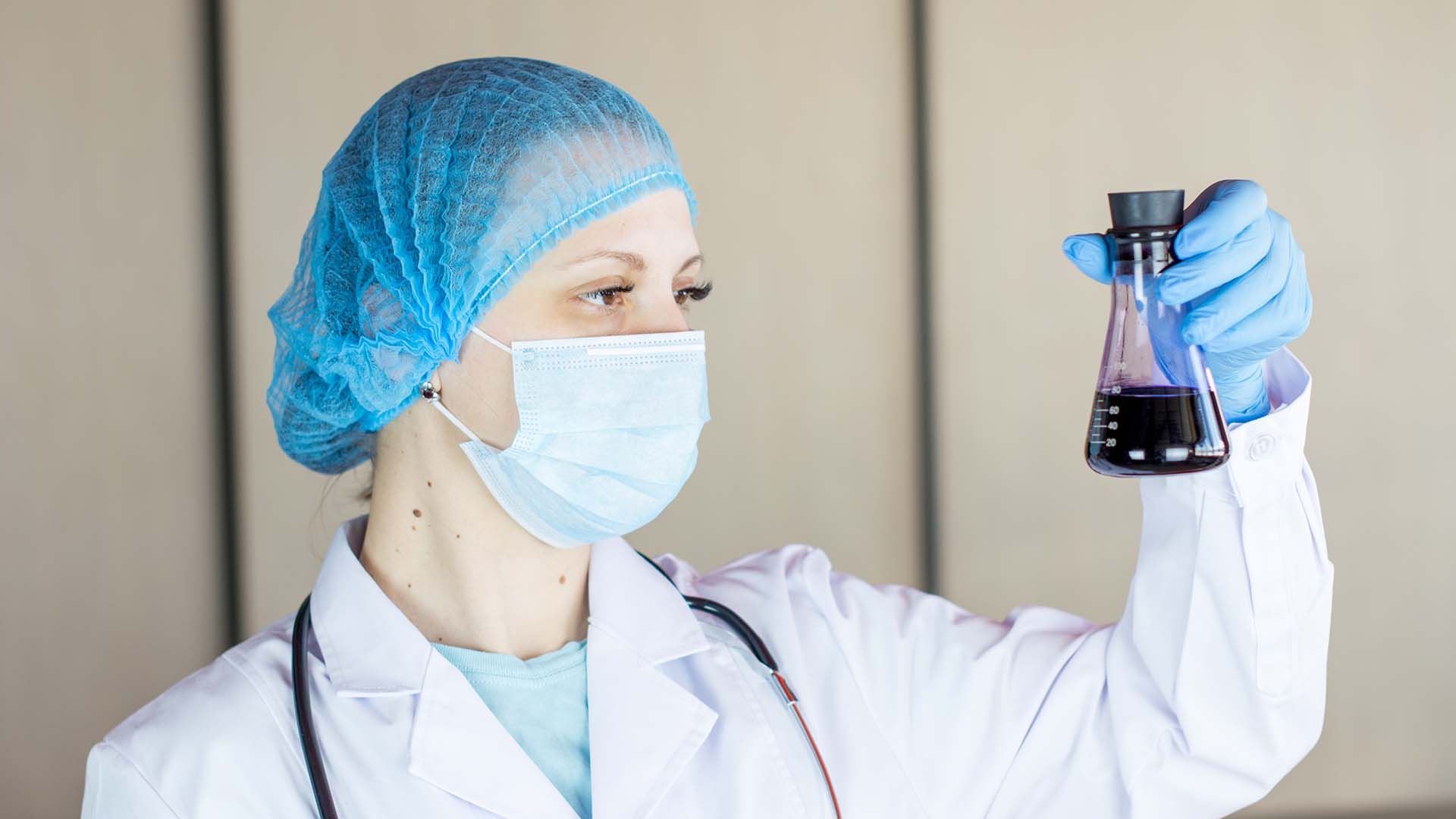 female doctor in PPE holding a laboratory flask