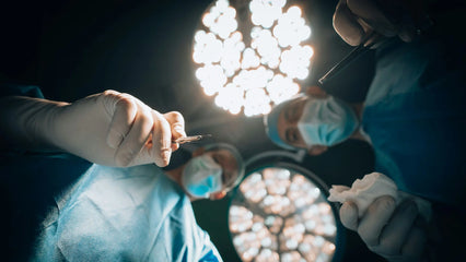 View of a patient lying on the bed with the surgical team in personal protective equipments looking and a medical light above their heads.