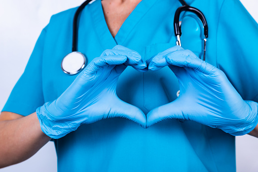 a medical professional in scrub suit with a stethoscope on neck while making a heart sign with their hands