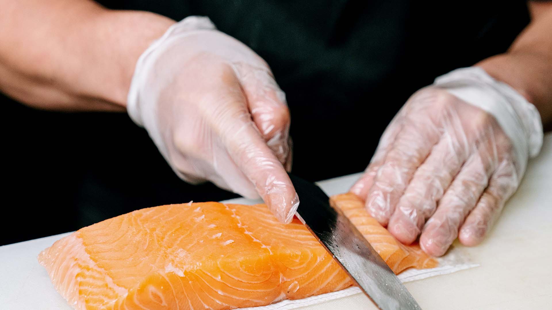 chef wearing clear vinyl gloves while slicing a raw salmon