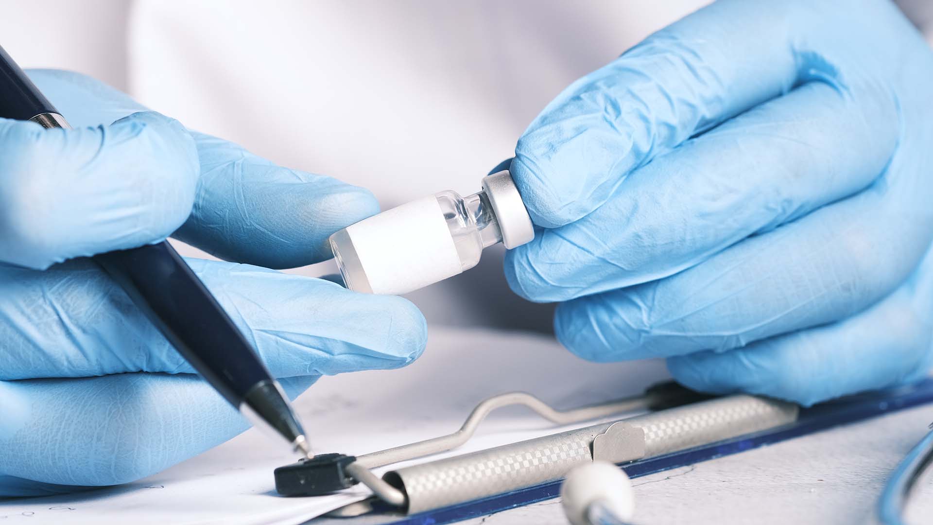 person in blue nitrile gloves holding a vial