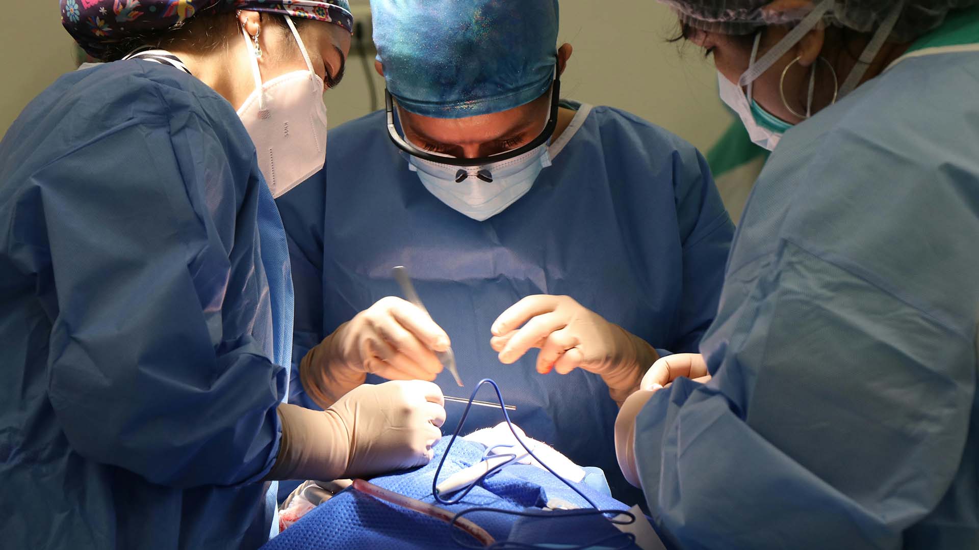 a surgeon with two medical assistants performing a surgery