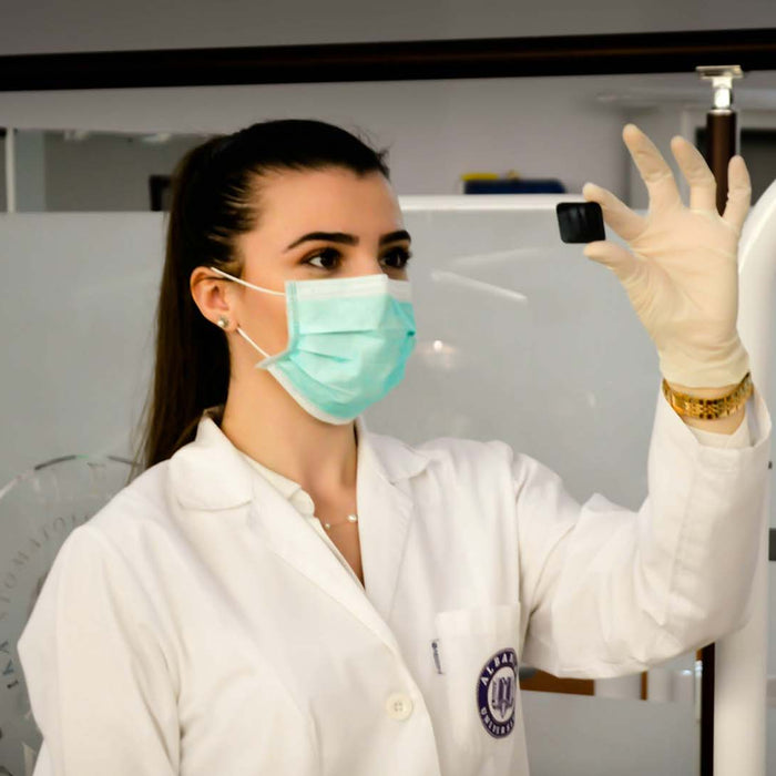 A dentist in lab coat and mask holds something up in front of her while wearing gloves.