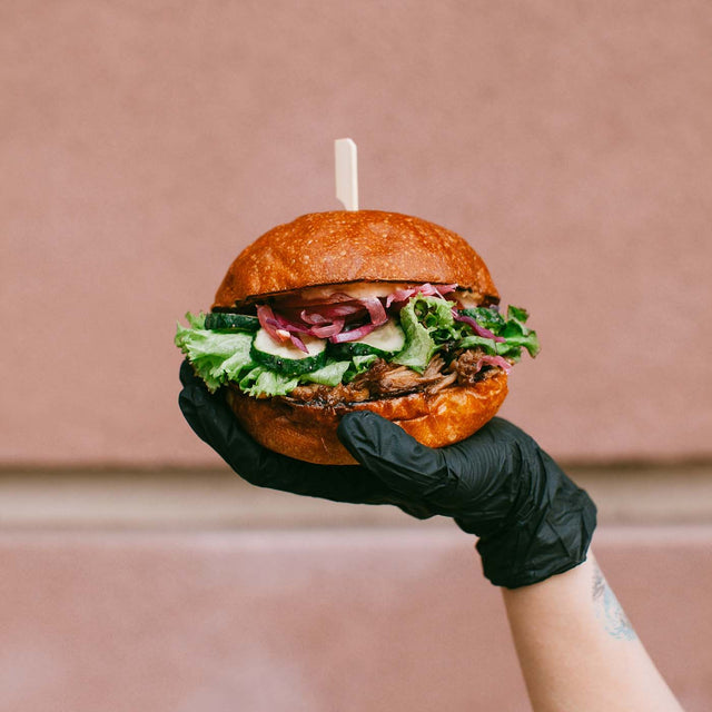 person wearing black gloves and holding a hamburger