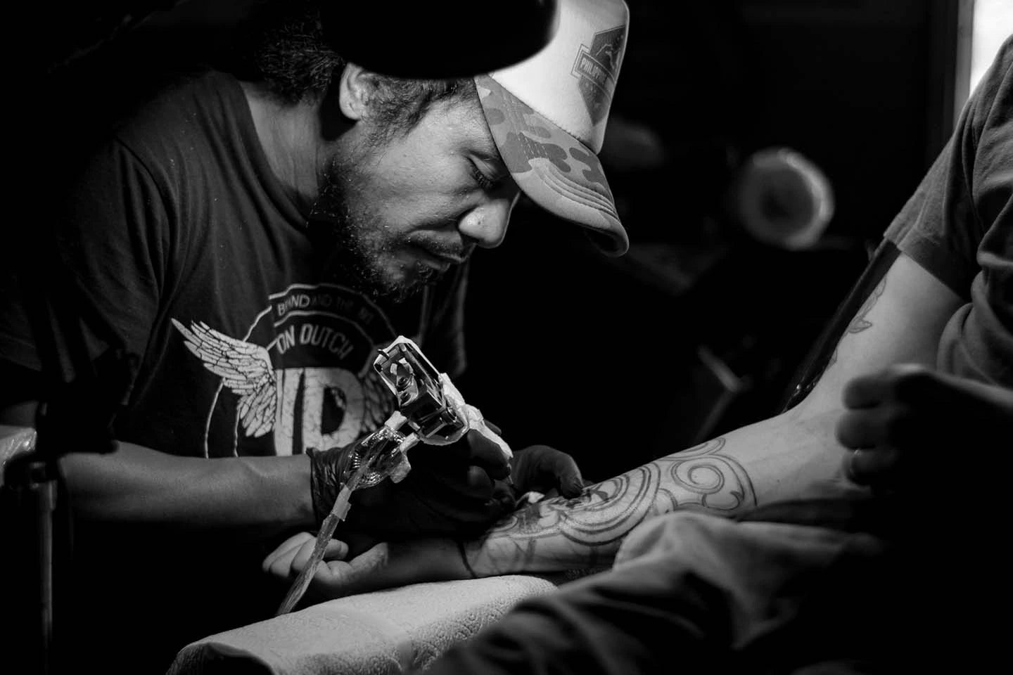 grayscale photo of an artist doing tattoo while wearing black gloves