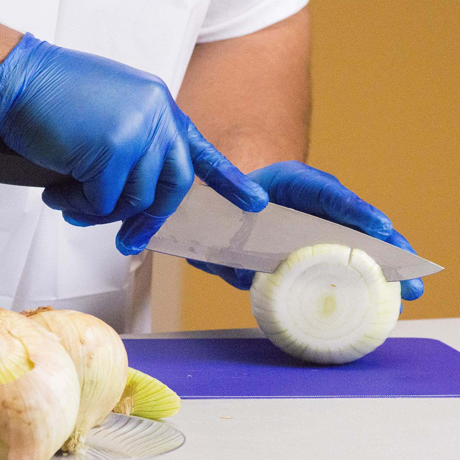 person wearing blue vinyl gloves while slicing a food