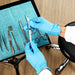 Medical professional wearing blue nitrile gloves holding syringe while preparing an examination tray
